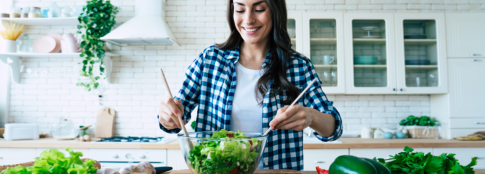 Smiling woman tosses fresh green salad in a bright kitchen.