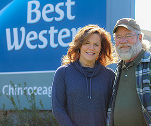 Lisa and Scott Chesson of Best Western Chincoteague smile beside their business sign.