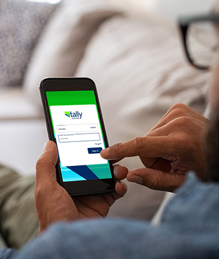 Man lying on sofa viewing Tally by Taylor Bank login screen from smartphone.