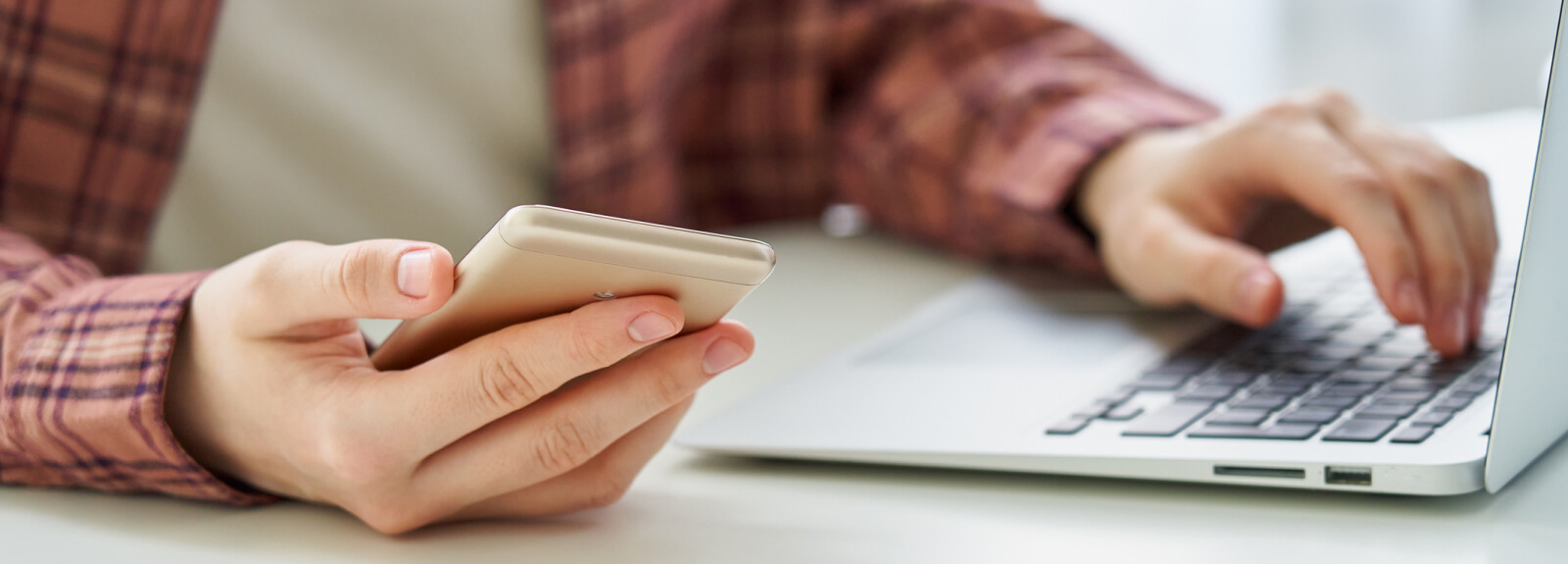 Close up of a person's hands with a phone and laptop