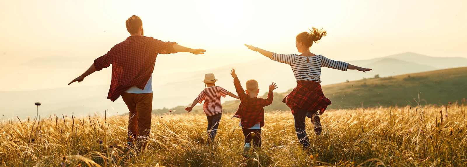 A young family playing in a large field with the sun behind them