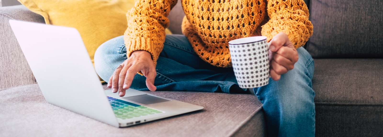 Close up of a person's hands using a laptop and holding a coffee cup